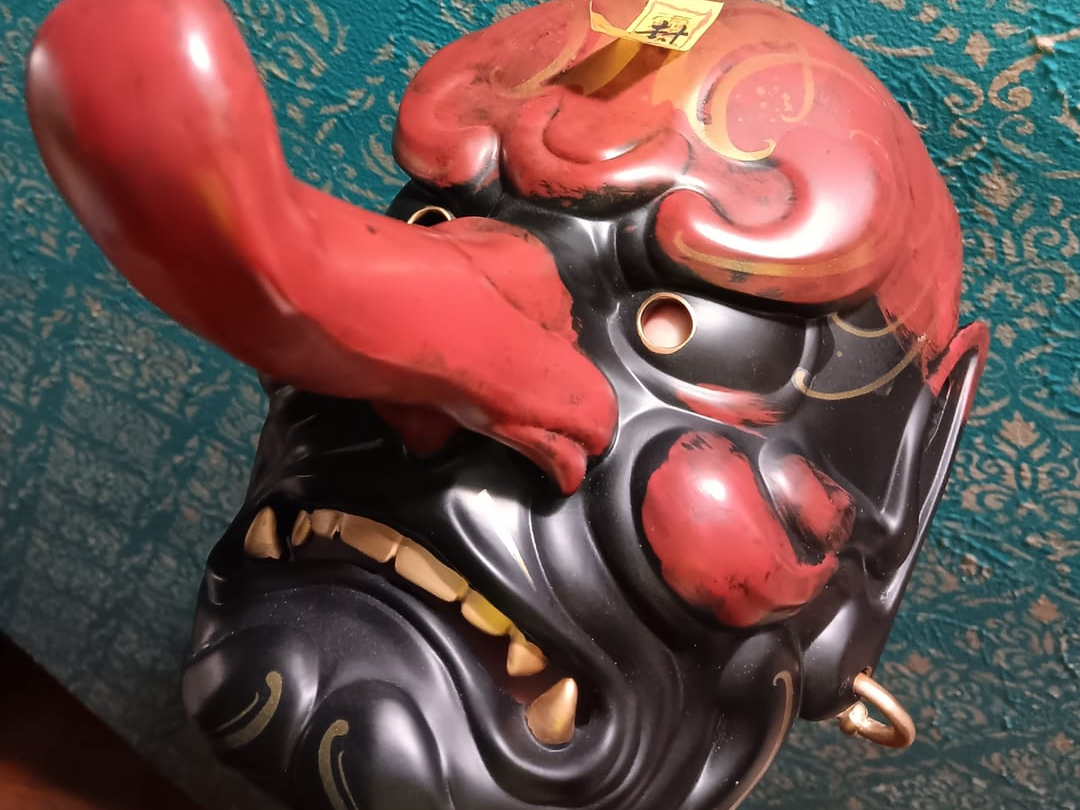 Close-up of a red and black Hannya mask on a patterned surface.